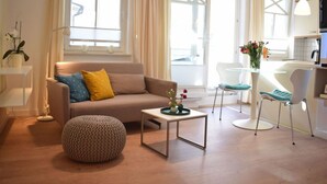 A modern living room with a sofa, ottoman, coffee table, and a dining area with a chair and table. - Sandpiper in Haus Strandburg Binz (Binz)
