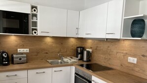 A modern kitchen with white cabinets, a wooden countertop, a built-in oven, a microwave, a coffee maker, and a toaster. - Sandpiper in Haus Strandburg Binz (Binz)