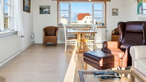 A living room with a dining area, a brown leather chair, a white sofa, and a view of a house through large windows.