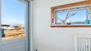 A room with a large window, a white chair, and a wooden shelf with a plant.