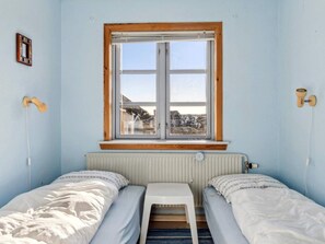 A small room with two single beds, a window with a wooden frame, a radiator below the window, and a small table in the center. - 4 Person Holiday Home in Frostrup (Frøstrup)