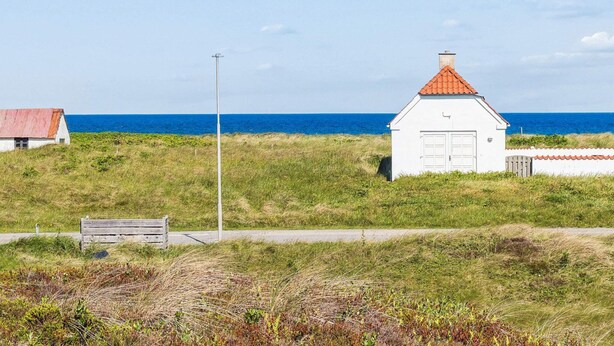 A coastal scene with a white building with a red roof, a street lamp, and a bench.