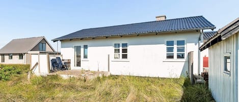 A single-story house with a dark roof and white walls, a front door, and a small porch area.