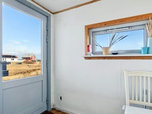 Una habitación con un ventanal grande, una estantería de madera con una planta en maceta y una silla blanca.