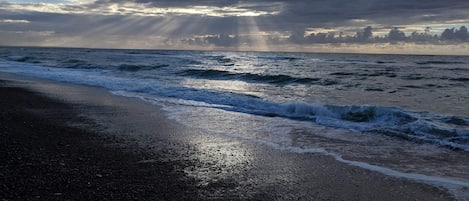 Une plage avec des vagues, un ciel nuageux et la lumière du soleil.