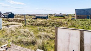 A coastal landscape with several houses, a wooden fence, and a clear sky.