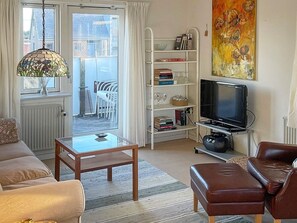Een woonkamer met een bank, een salontafel, een televisie, een boekenkast en een schilderij.