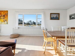 A dining area with a wooden table and chairs, a window with curtains, and artwork on the walls. - 4 Person Holiday Home in Frostrup (Frøstrup)