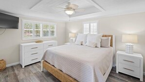 A bedroom with a bed, white nightstands, a ceiling fan, and a window with blinds. - 6150 Midnight Pass Road Villa 40B (Sarasota)