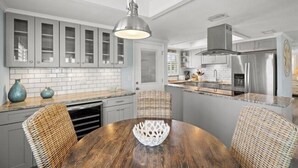 A modern kitchen with white cabinets, a stainless steel refrigerator, and a dining area with a wooden table and wicker chairs. - 6150 Midnight Pass Road Villa 40B (Sarasota)