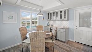 A kitchen with a dining area, featuring wicker chairs, a round table, and white cabinets. - 6150 Midnight Pass Road Villa 40B (Sarasota)