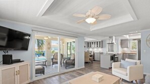A spacious living area with a flat-screen TV, a ceiling fan, and a sliding glass door leading to a patio with outdoor furniture. - 6150 Midnight Pass Road Villa 40B (Sarasota)