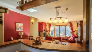A cozy kitchen with a wooden counter, a dining area with red upholstered chairs, and a view of the outdoors through large windows. - House 4 rooms 10 Pax, Fireplace, Garden & BBQ on the Slopes (La Molina)