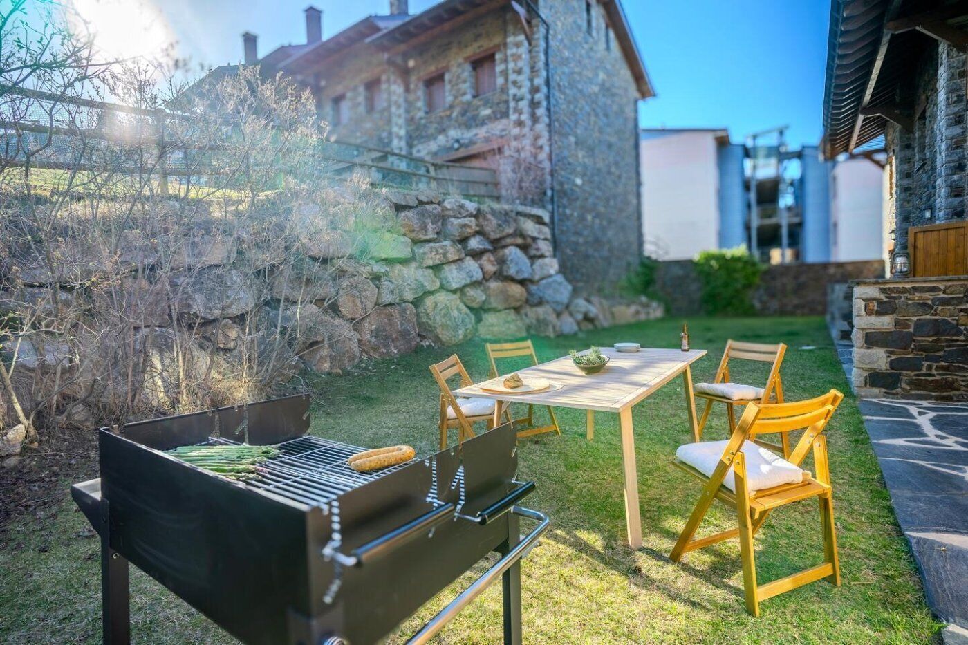 Un patio trasero con una parrilla, una mesa de comedor con sillas y un muro de piedra.