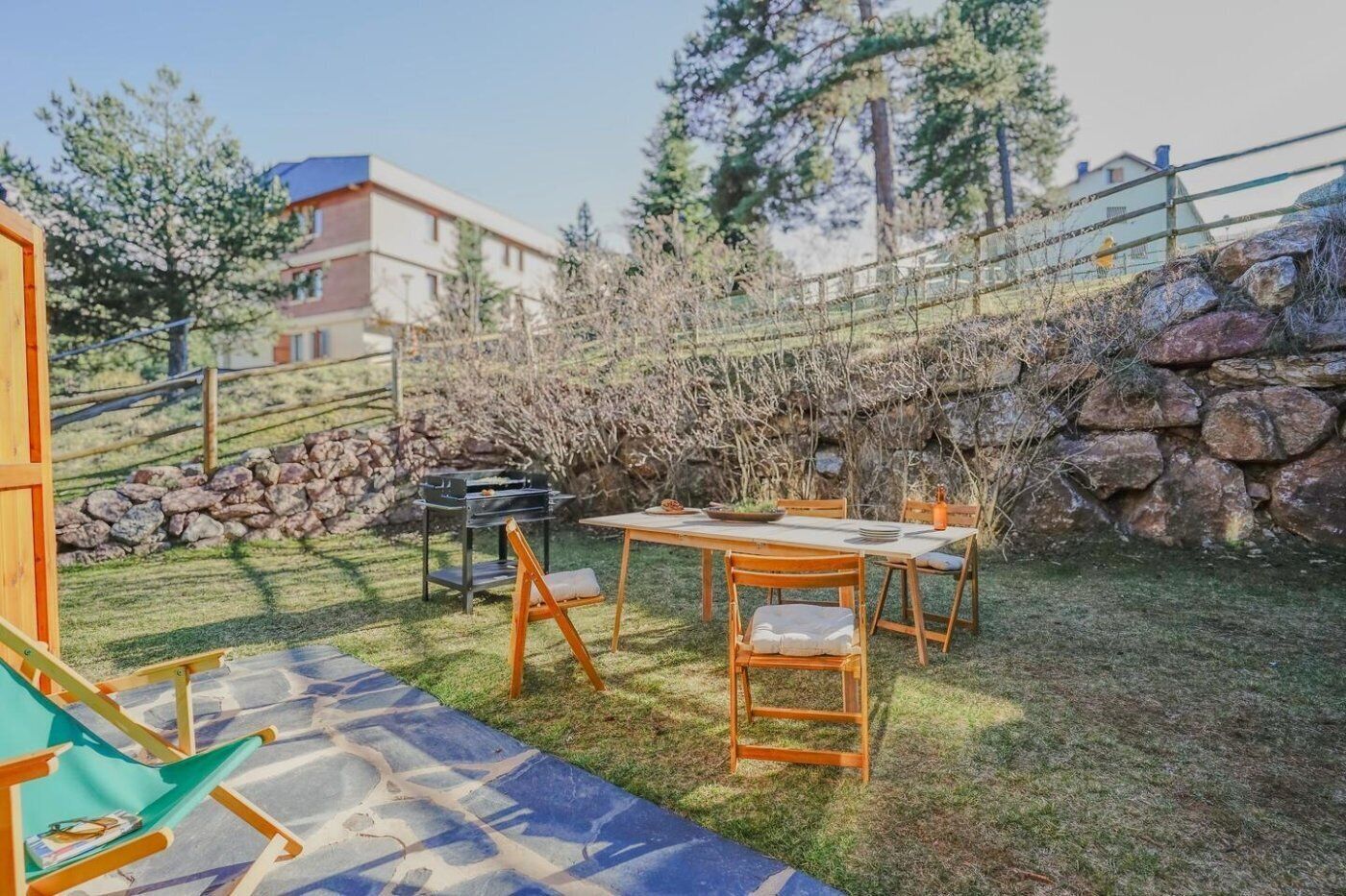Een terras buiten met een tafel, stoelen, een barbecue en een stenen muur.