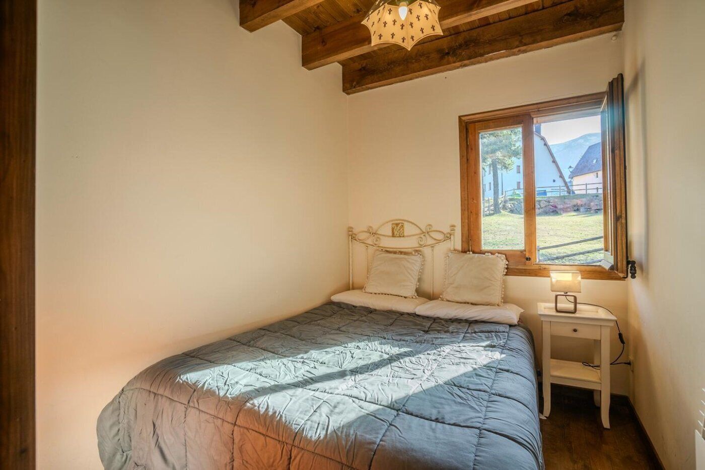 Une chambre à coucher avec un lit, une table de chevet, une fenêtre donnant sur un beau paysage et des poutres en bois au plafond.
