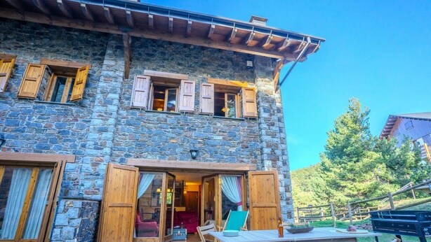 A stone building with wooden shutters, a patio with a table and chairs, and a view of trees. - House 4 rooms 10 Pax, Fireplace, Garden & BBQ on the Slopes (La Molina)