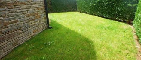 A well-maintained garden with a stone wall, neatly trimmed grass, and a hedge.