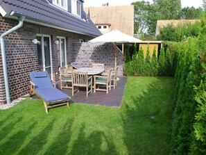 A patio area with a table and chairs, a sun lounger, and a covered seating area.