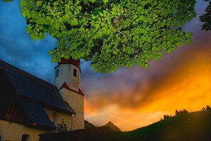 A church with a clock tower, surrounded by greenery and a dramatic sky. - Apartment in Damuls Near Ski Slopes (Damüls)
