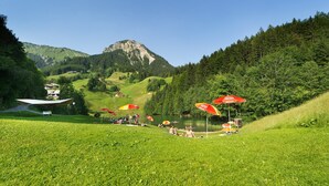 Uma área gramada com guarda-sóis vermelhos, uma montanha ao fundo e alguns edifícios.