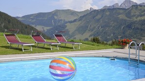 Piscina com espreguiçadeiras e uma bola de praia, cercada por montanhas.