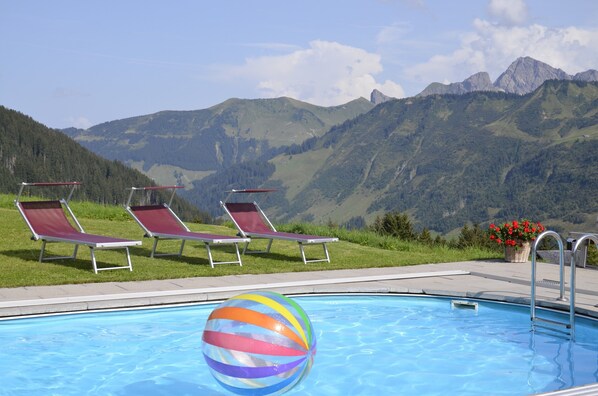 Ein Schwimmbecken mit Liegestühlen und einem Strandball, umgeben von Bergen.