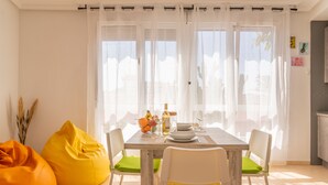 A dining area with a wooden table set for four, white chairs with green cushions, and two yellow bean bags. - Your oasis of peace in Corralejo, views of the ocean and volcanoes. Top pool! (Corralejo)