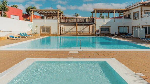 A swimming pool with a wooden deck, lounge chairs, and a covered area with a balcony. - Your oasis of peace in Corralejo, views of the ocean and volcanoes. Top pool! (Corralejo)
