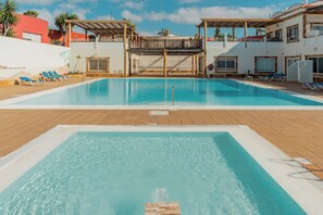 En swimmingpool med træterrasse, liggestole og et overdækket område med balkon.