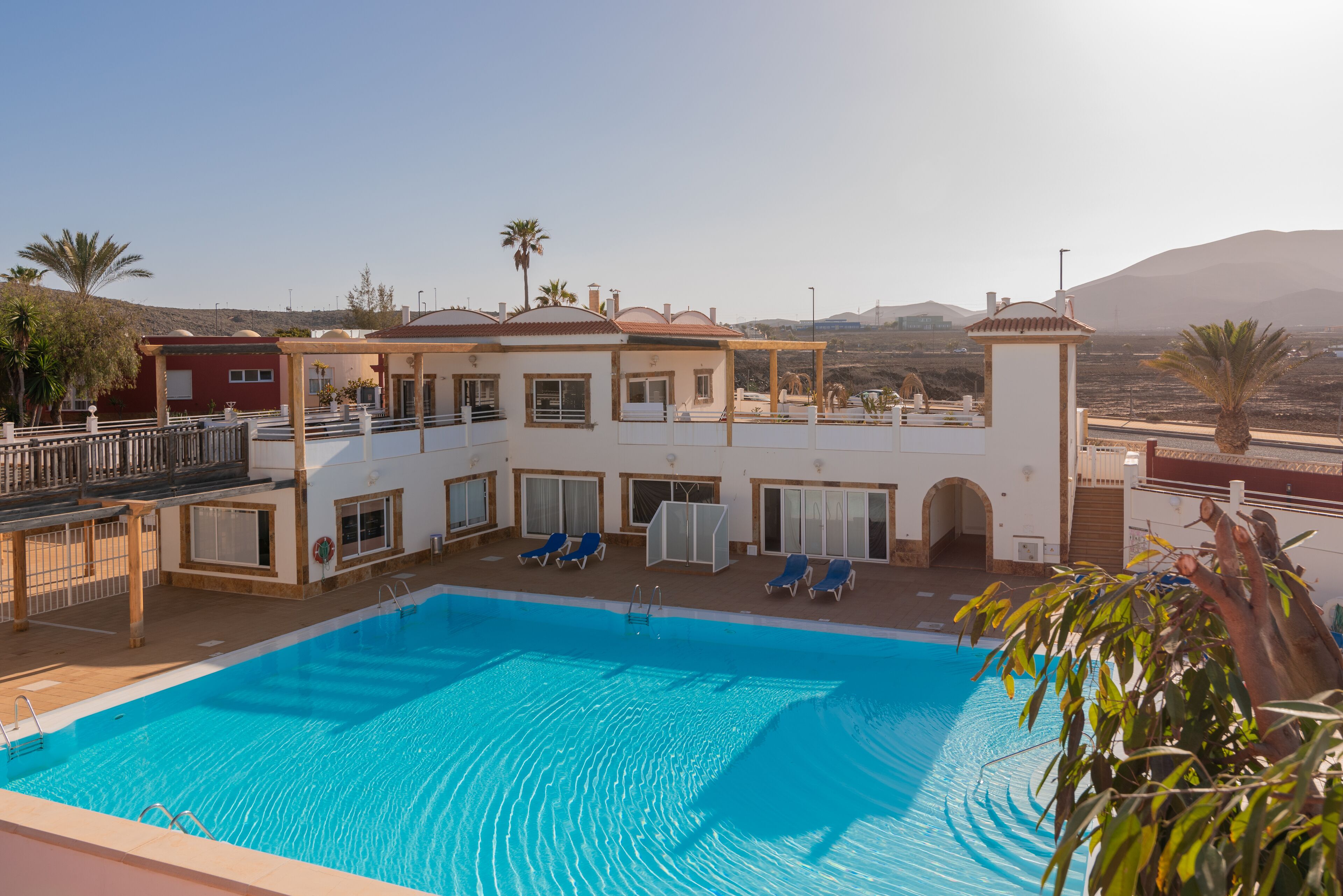 A pool area with a clear view of the pool, lounge chairs, and a building with multiple windows and balconies.