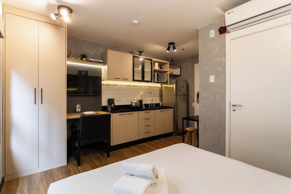 A compact hotel room with a bed, a small desk, a kitchenette, and a wardrobe.