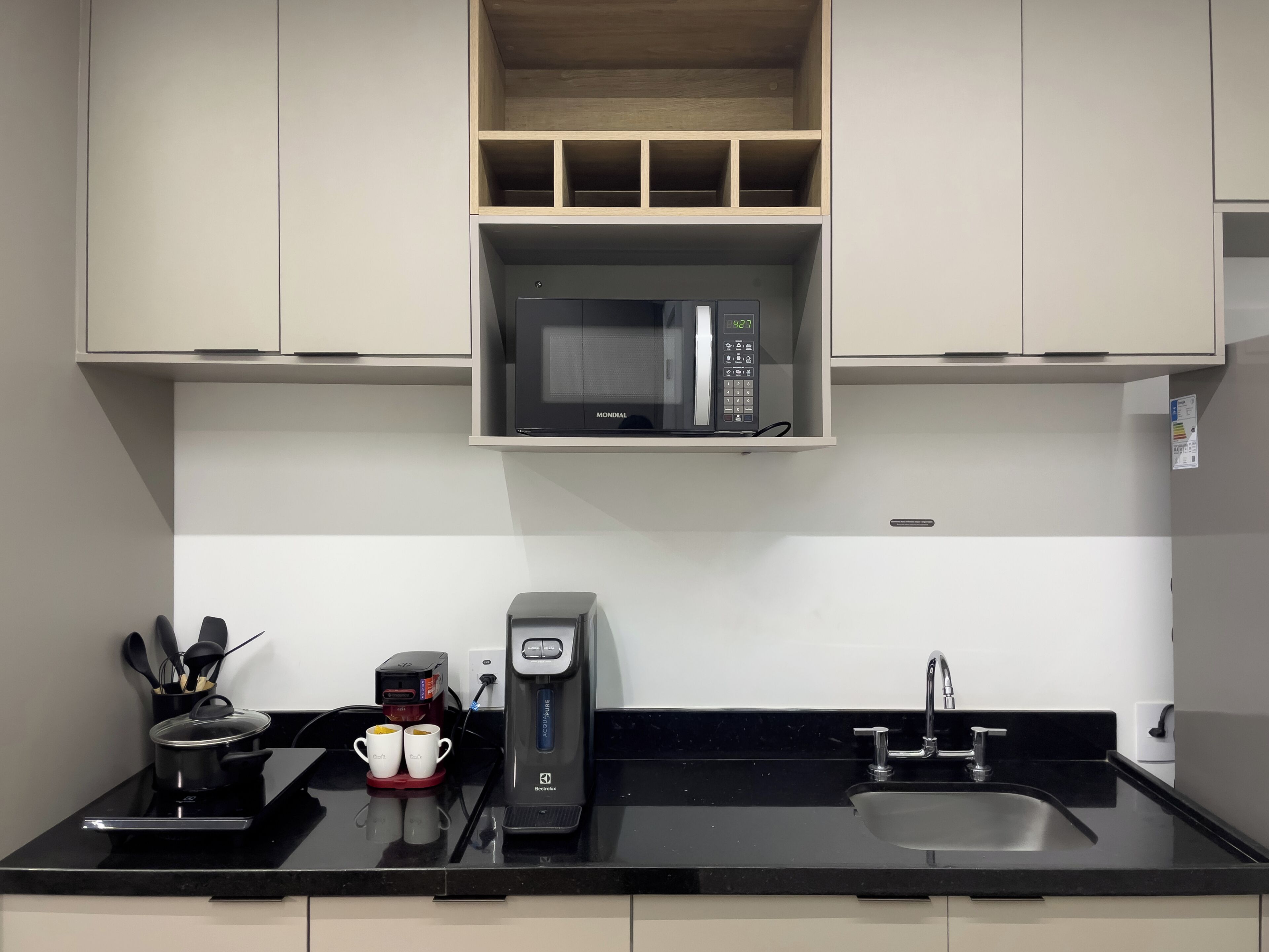 A kitchen with a microwave, coffee maker, sink, and utensils.