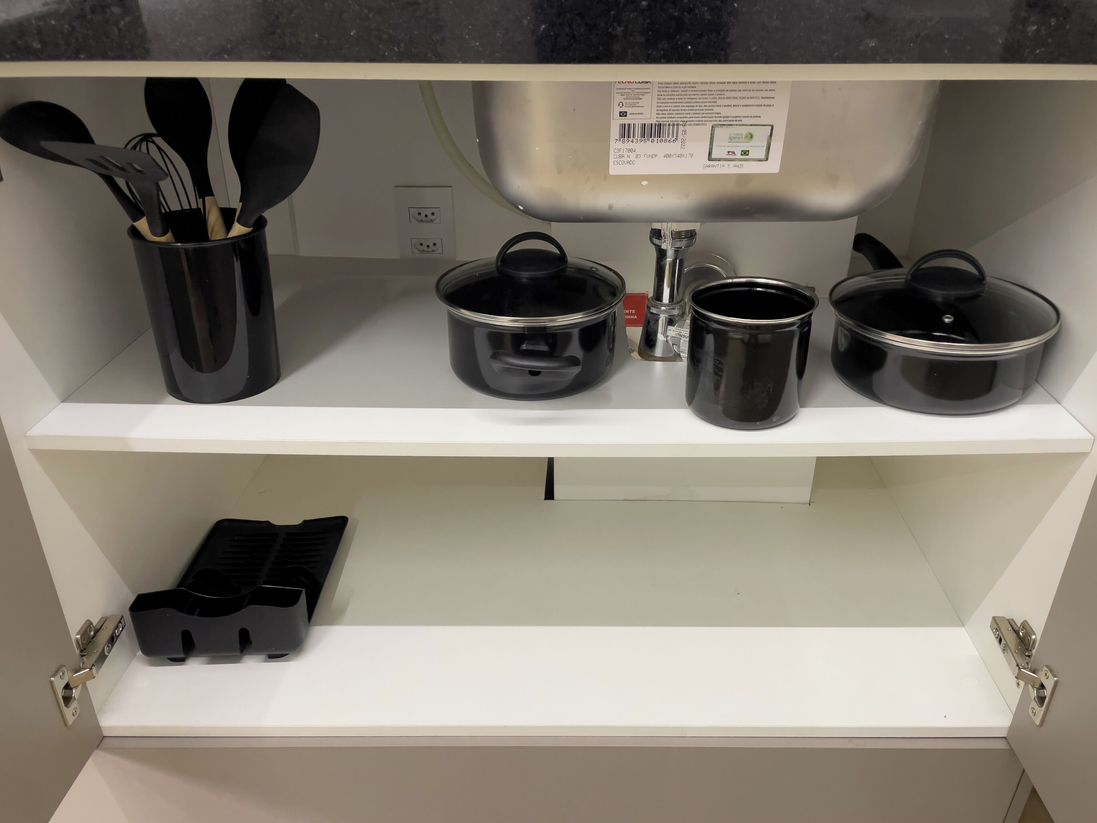 A kitchen shelf with black cookware, a utensil holder, and a kettle.