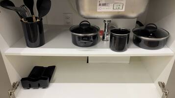 A kitchen shelf with black cookware, a utensil holder, and a kettle.