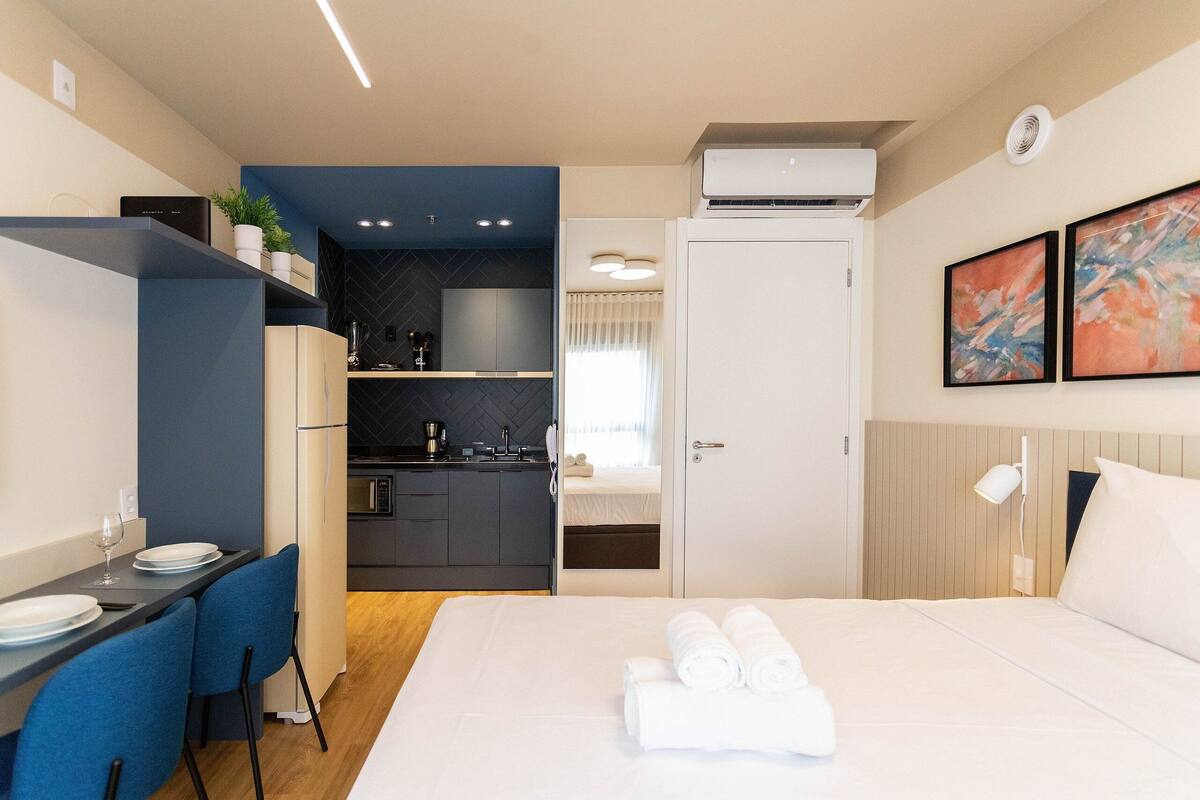A modern hotel room with a bed, a dining area, and a kitchenette.