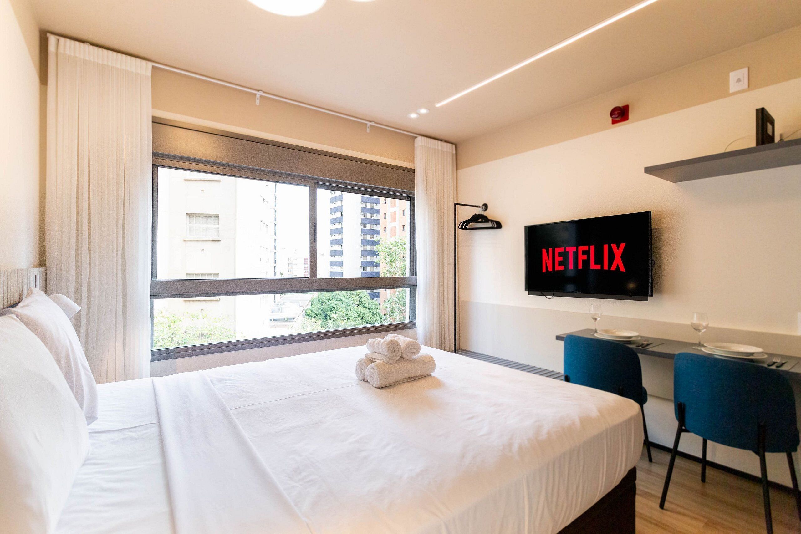A hotel room with a bed, a desk with a chair, a television, and a window with curtains.