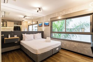 Una habitación de hotel moderna con una cama grande, un escritorio integrado, un televisor y un ventanal con vistas a zonas verdes.