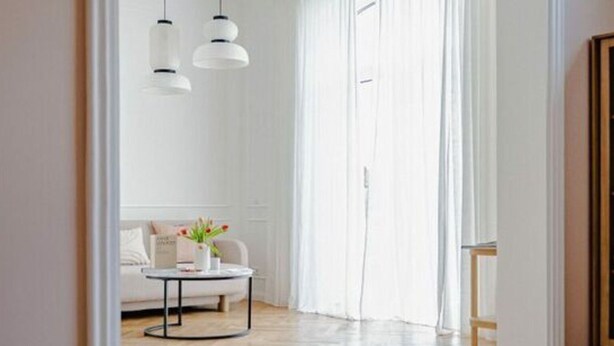 Un salon moderne avec un plancher en bois, des murs blancs et un canapé blanc. Deux suspensions sont accrochées au plafond.