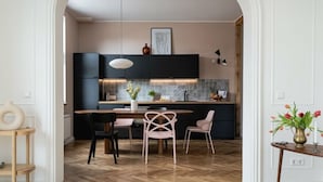 Une cuisine moderne avec des meubles de couleur sombre, une table à manger en bois et deux chaises roses.