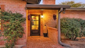 A brick building with a well-lit entrance, a chimney, and a door with a window. - Private Foothills Villa + Panoramic Views + Heated Pool/Spa (Tucson)