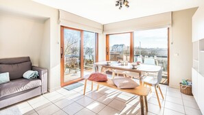 A bright room with a sliding glass door leading to a balcony, a wooden table with chairs, and a grey sofa. - Apartment in Oostduinkerke Near the Beach (Koksijde)