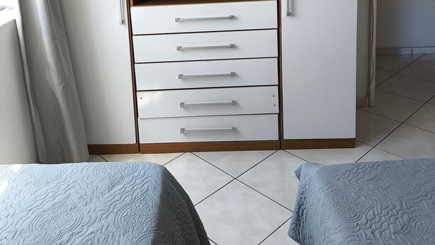A bedroom with a wardrobe, two beds, and a window with curtains. - Apartamento Charmoso a 100 m da Praia Grande Arraial do Cabo (Arraial do Cabo)