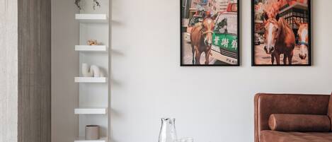 Ein modernes Wohnzimmer mit einem Glastisch, einem braunen Sofa und zwei gerahmten Gemälden von Pferden an der Wand.