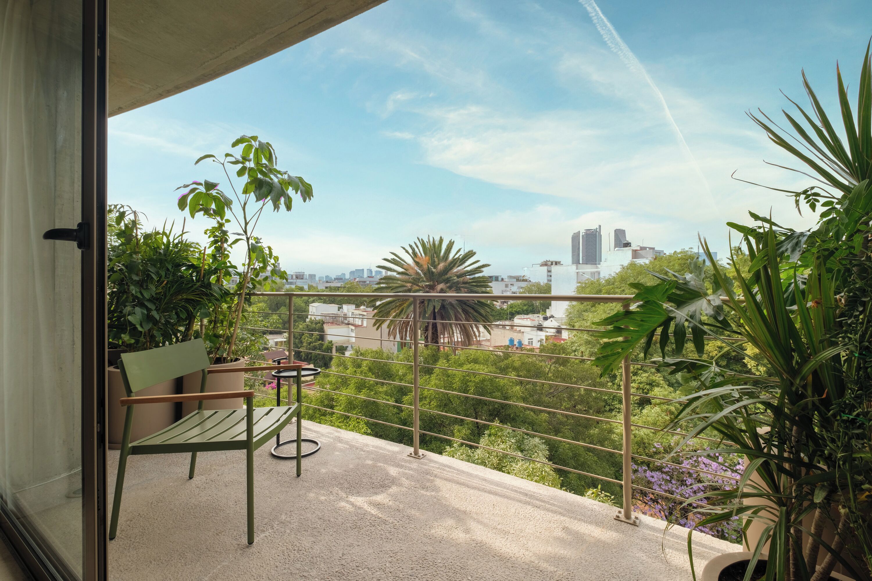 A balcony with a view of a cityscape, a chair, and potted plants.