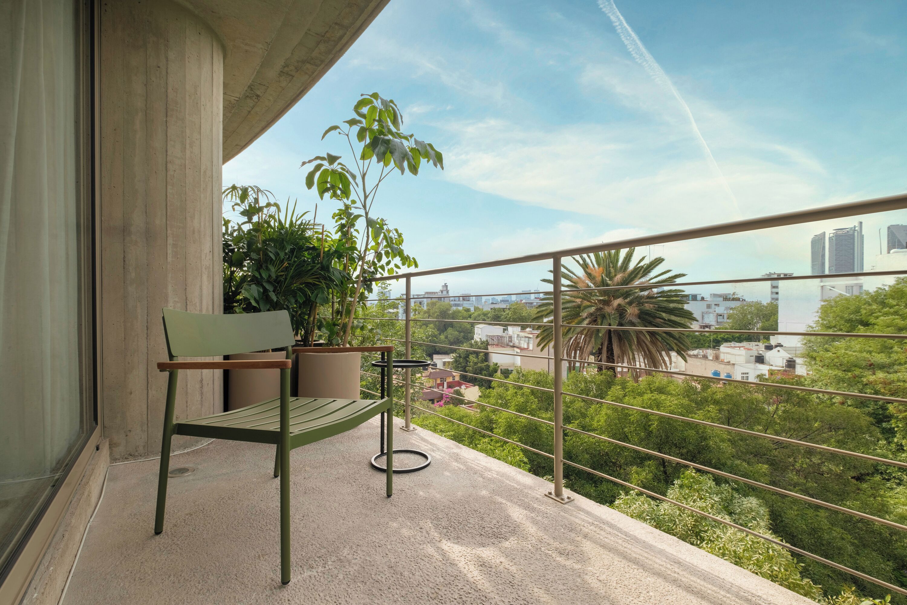 A balcony with a green bench, potted plants, and a city view.