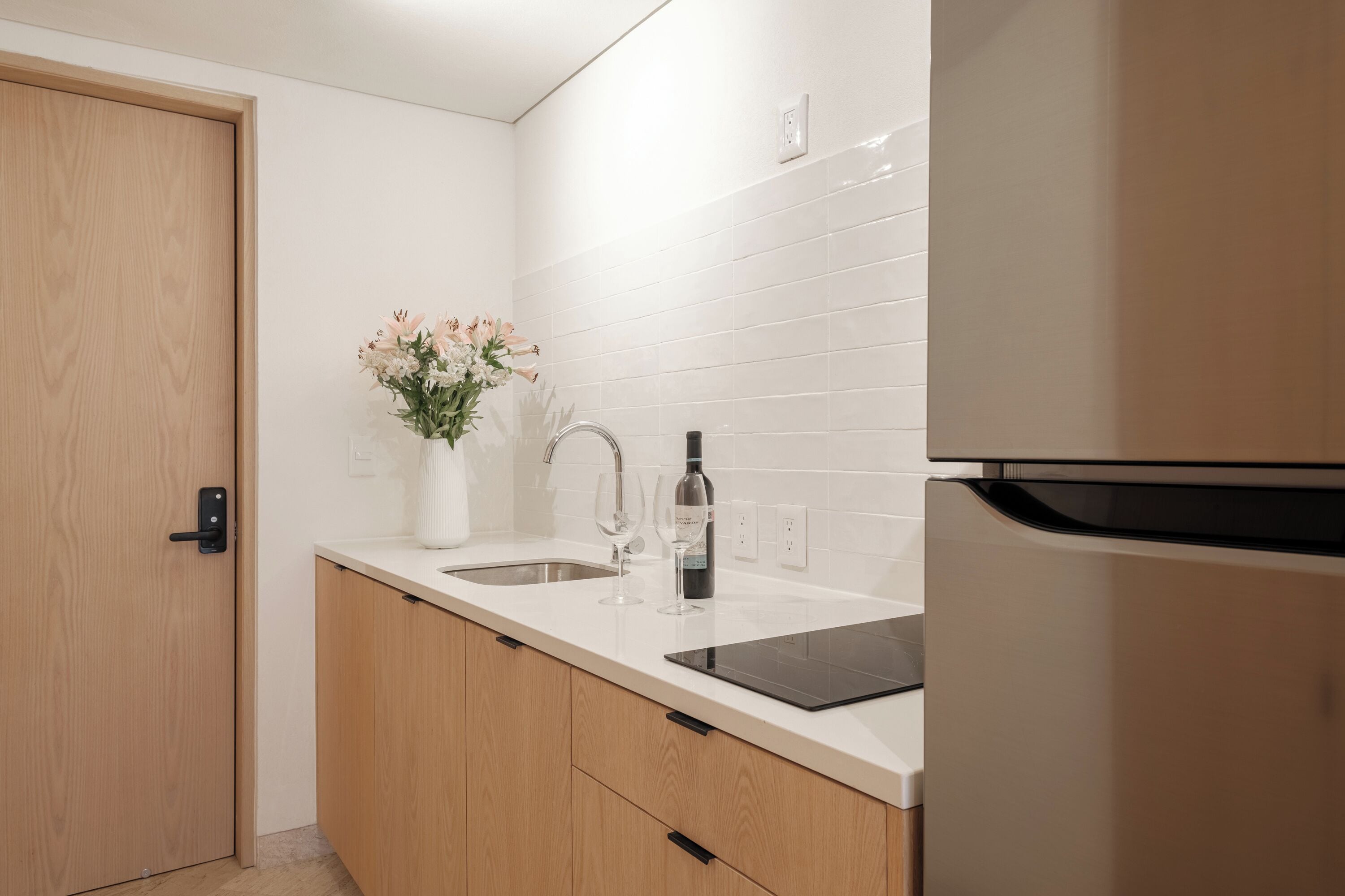 Une cuisine moderne avec des carreaux blancs, des armoires en bois, un réfrigérateur en acier inoxydable et un vase rempli de fleurs posé sur le plan de travail.