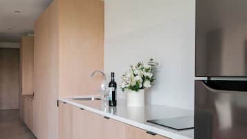 A modern kitchen with wooden cabinets, a stainless steel refrigerator, a wine bottle, and a vase with flowers on the counter.