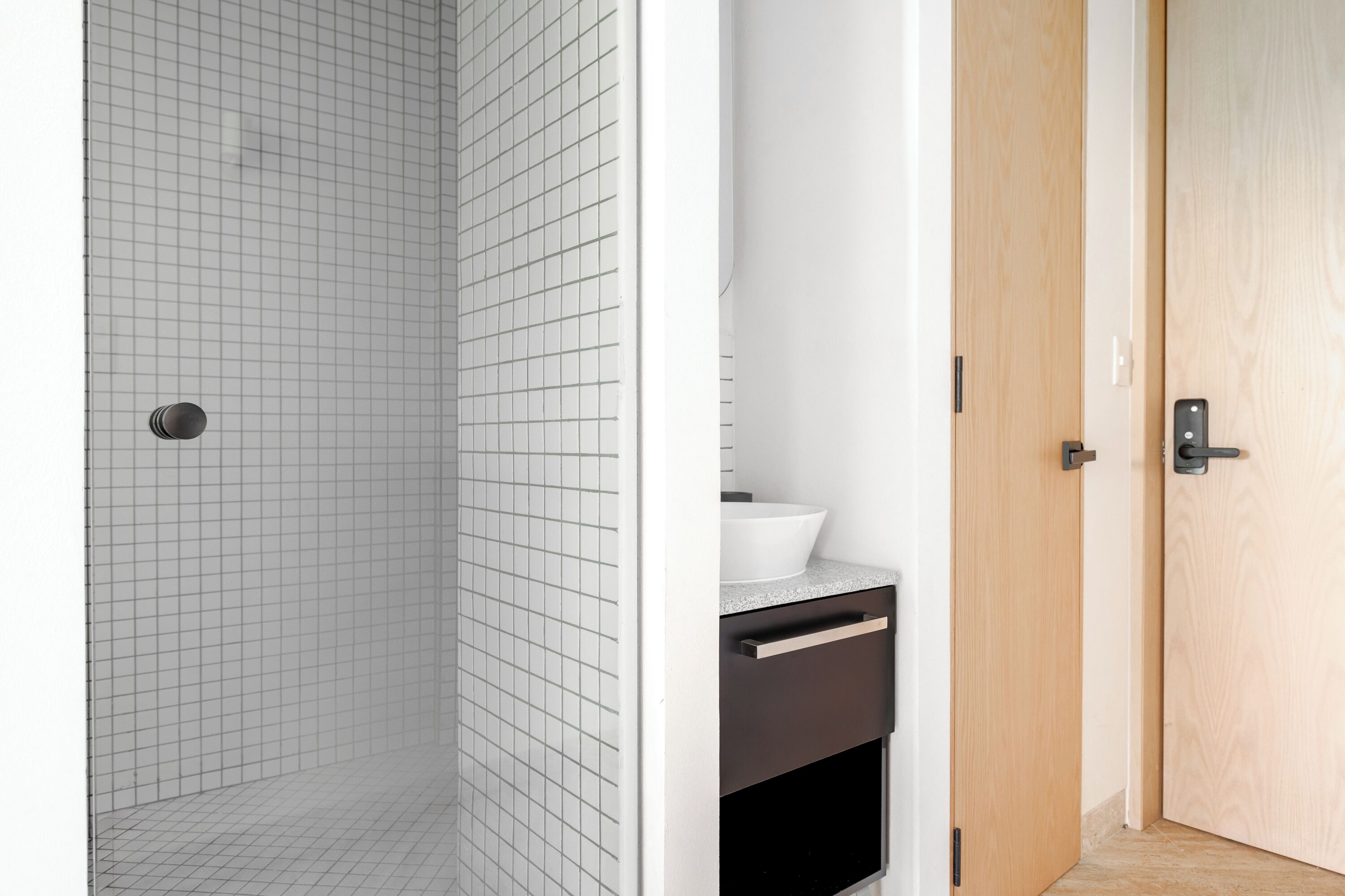 Une salle de bain avec une douche carrelée, un lavabo blanc et une porte en bois.