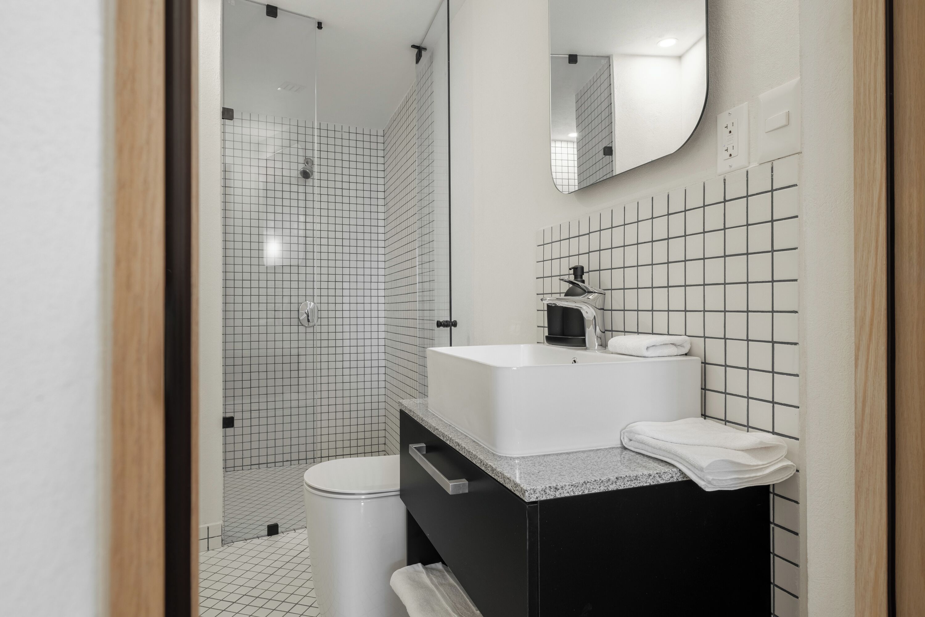 A modern bathroom with a white sink, black vanity, and a glass shower enclosure.